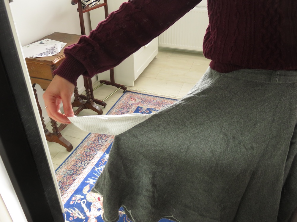 Grey skirt with pocket back turned out and held out at arm's length, showing that the pocket is too low and too small